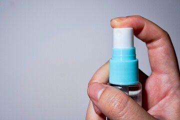 Close up human finger pressing on blue bottle spray isolated on horizontal copy spaced plain background.