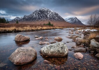 Mountain stream flows through autumnal landscape, snow-capped peak