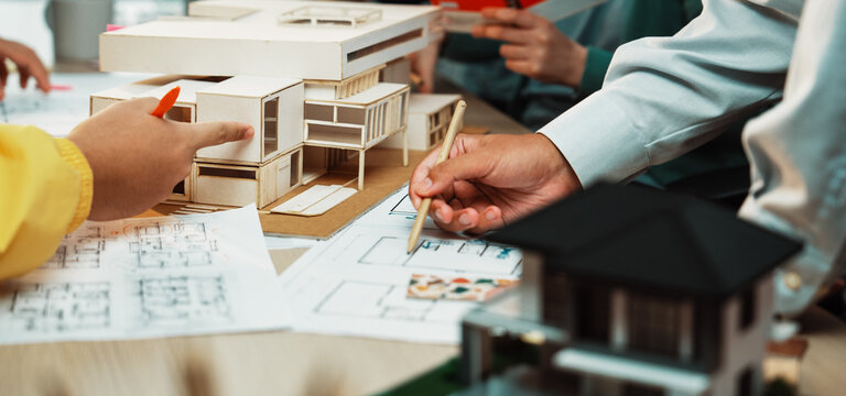 A vibrant architecture studio scene showing professionals engaged in model building and discussion. Various design sketches and physical models illustrate creative processes and teamwork. SACTR - Powered by Adobe