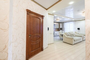 interior view with a wooden door on the left, wallpapered walls, and a glimpse of a living space with a sofa and kitchen in the background