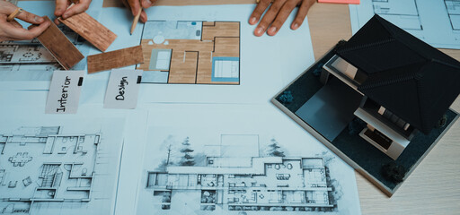 A collaborative scene showing diverse professionals engaging in architectural planning, with blueprints and a scale model laid out on a table for design analysis. SACTR