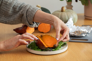 Female preparing sweet potato on cutting board with squash in background