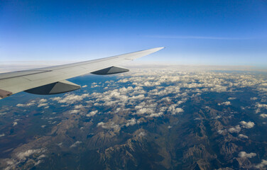 Obraz premium View through an airplane window catching the amazing mountains through the clouds, with the plane's wing prominently displayed against the horizon.