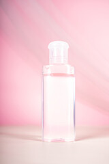 Generated ImA clear plastic bottle with transparent liquid, standing on a light surface with a pink fabric background, creating a soft and elegant look.age