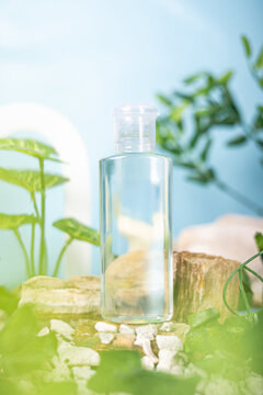 Generated ImagA clear cosmetic bottle filled with transparent liquid, placed among natural elements with green leaves and wooden pieces on a blue background.e