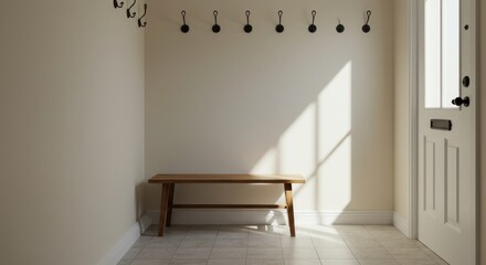 Interior shot of a sunlit entryway. A simple wooden bench sits beneath a row of hooks on a blank wall. A door is partially visible on the right