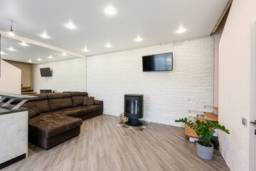 modern living room features a brown sectional sofa, a sleek fireplace, a TV mounted on a white textured wall, and wood-look tile flooring. Natural light and plants add warmth