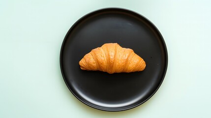 A Single Croissant on a Round Black Plate