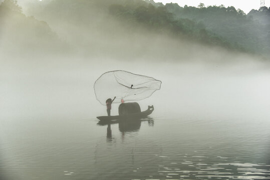 Solitary Fisherman Casting Net From Boat On Foggy Xiao Dongjiang Lake In Chenzhou Hunan
