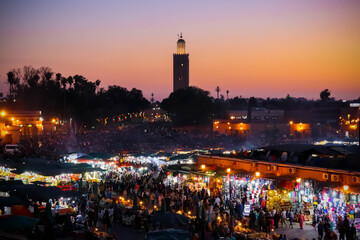 Sunset at Marrakesh square, Morocco, with warm golden light, bustling market stalls, local vendors, and the vibrant atmosphere of the city&rsquo;s historic heart.