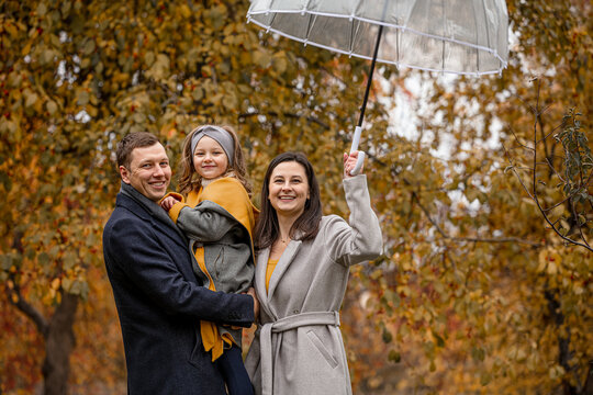 Family mother, father, daughter, beautiful happy together in autumn in nature with an umbrella under a leaf fall