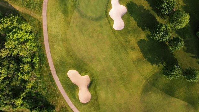 Patterned golf course greens and fairways with sand bunkers viewed from above, drone top down pan