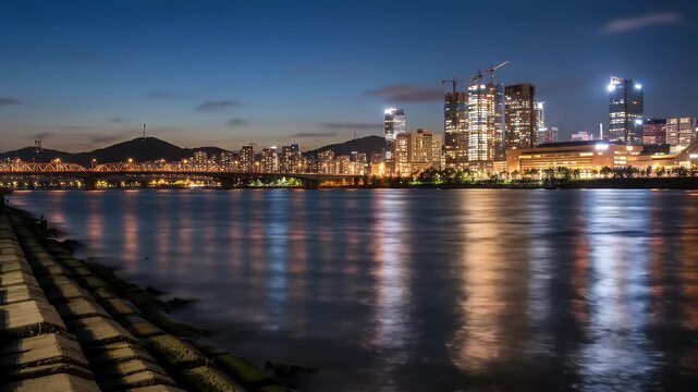 Panoramic Night Cityscape Reflection with Illuminated Buildings Along the Riverbank Under a Blue Sky at Twilight Offers a Captivating View of Urban Charm and Architectural Splendor
