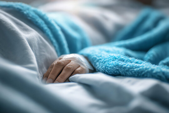Hand with an intravenous catheter resting on a blue blanket, indicating medical treatment or hospital care. - Powered by Adobe