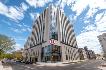 Obraz premium Modern multi-story commercial building with glass and concrete facade under a partly cloudy sky.