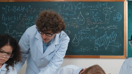 Caucasian smart teacher support excited curious student pour colored liquid in beaker at laboratory. Creative children concentrate to do experiment and enjoy inspecting biochemical sample. Pedagogy.