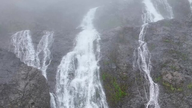 Aerial shot of beautiful waterfall from above the mountains surrounded by trees