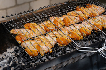 Delicious chicken frying on barbecue grill grate outdoor. Seasoning falling on fresh grilled chicken wings. Summer party food ideas. BBQ Juicy roasting chicken grill legs on grill grate 
