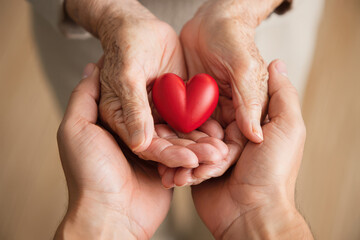 Obraz premium Two pairs of hands gently holding a red heart symbol