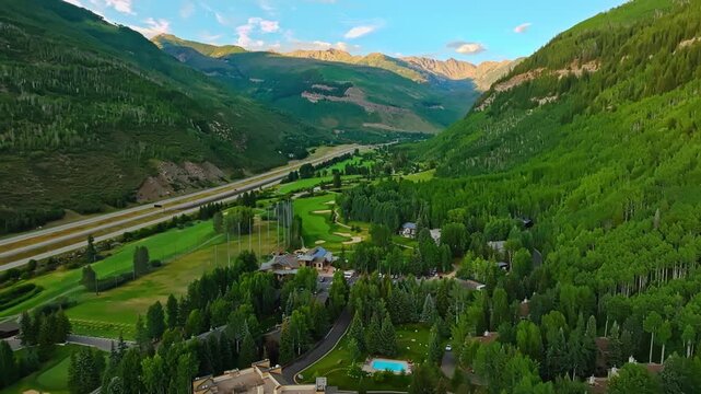Drone tracking left tilt up along golf course of open Vail landscape with winding mountain road and sparse tree cover