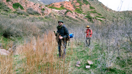 A male guide guides a tourist through an unexplored wilderness by following a map on his phone. Two people walk through a field along mountains