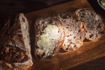 Spread butter on sliced ​​cranberry walnut sourdough bread and place on wooden cutting board.