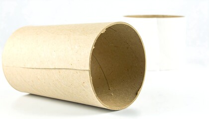 A tan cardboard tube rests on a white background, another tube blurred in the background