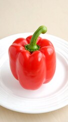 A single, vibrant red bell pepper sits on a simple white plate against a beige backdrop