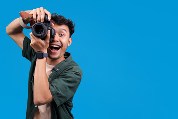 Obraz premium Excited Male Photographer Holds A Camera, Taking A Picture With Smiling, Isolated On Blue Background