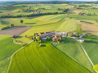 Aerial view of farm house in Switzerland in Canton of Fribourg. Rural fields in evening sunlight.