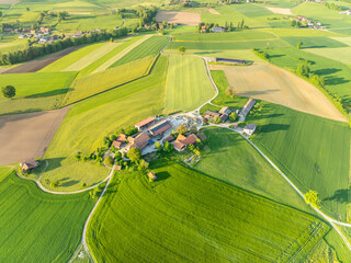 Aerial view of farm house in Switzerland in Canton of Fribourg. Rural fields in evening sunlight.