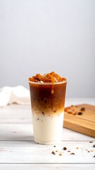 Iced coffee drink in a clear plastic cup with caramel topping, served on a white wooden surface
