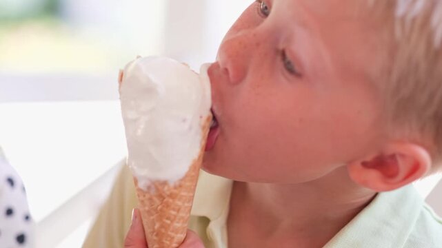 close up portrait blond caucasian boy eating and enjoying ice cream in waffle cone cup. summer holiday