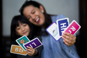 A mother and daughter sitting together on wooden steps, happily playing and learning with flashcards. Warm family bonding moment at home.