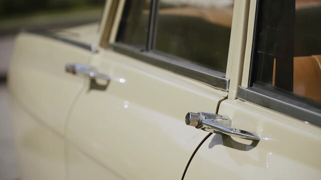 Chrome door handle with button of old vintage beige car on sunny day close up. Exterior of retro sedan from 80s in parking lot during journey.