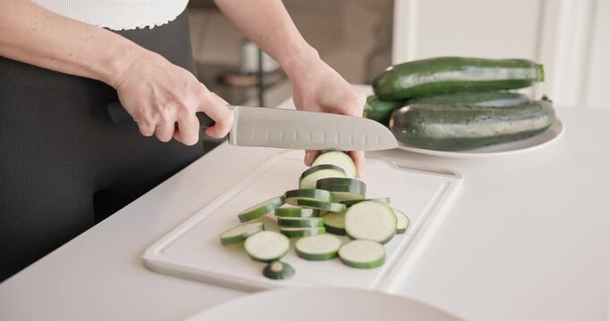 Home cooking - woman in small apartment cutting fresh organic zucchini with santoku knife on vegetable cutting board