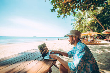 Digital nomad working on laptop with beach background