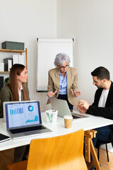 Vertical portrait of senior female boss talking to employees in the office.
