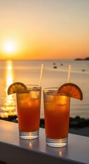 Two orange cocktails with orange slices and straws at sunset by the ocean