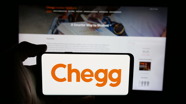Stuttgart, Germany - 08-18-2025: Person holding cellphone with logo of US edtech company Chegg Inc. on screen in front of webpage. Focus on phone display.