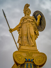 Statue of Athena, the Greek goddess of wisdom and knowledge, with a helmet, spear and shield on a gold gilded column. Craftsmanship highlights the power of the deity, set against a timeless backdrop.