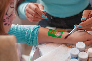 creating a Shimmering glitter tattoo on a child's hand at a birthday party. Mom makes a tattoo for her daughter. sparkling tattoo on a child's . Body art. bright sparkles at the party