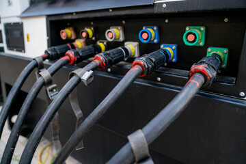 Electric power connectors with thick black cables attached to generator or distribution unit, colorful industrial sockets used in events, concert setup, stage energy supply technology
