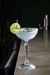 A beautifully crafted cocktail sits on a polished bar counter, adorned with lime and mint leaves