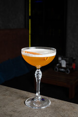 A vibrant cocktail in a coupe glass features an amber hue and a twist of orange peel