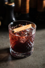 A deep red cocktail garnished with a cinnamon stick rests on an elegant surface, inviting warmth