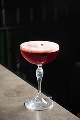 A beautifully crafted cocktail rests on a glossy bar surface, showcasing vibrant colors and foam