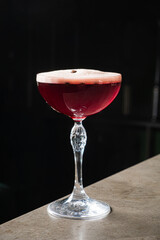 Deep red cocktail rests elegantly in a coupe glass on a polished bar surface, inviting savoring