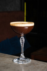 Dark coffee cocktail rests in a delicate glass, highlighting its frothy top and inviting appearance