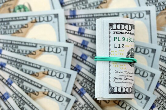 Roll of hundred dollar bills USD banknotes lies on big amount of united states money